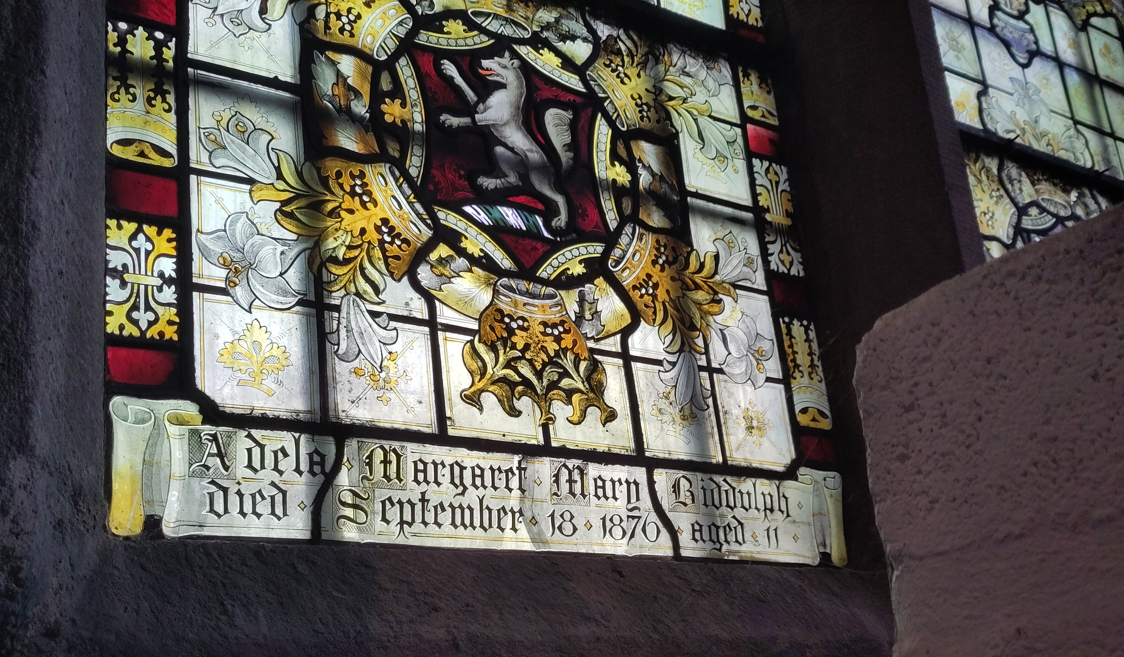 A photograph of an inscription on the window, painted in gothic lettering. It read 'Adela Margaret Mary Biddulph. Died September 18 1876 aged 11.